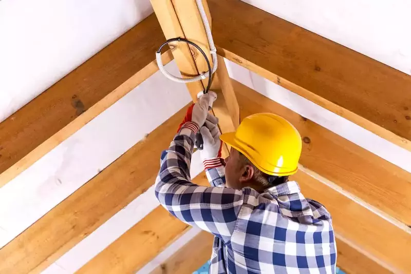 A licensed electrician working on the electrical installation of an attic fan