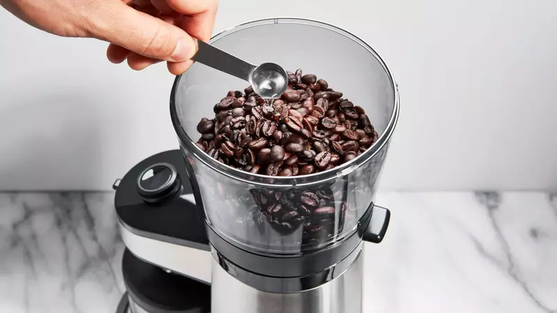 A coffee grinder with coffee beans scattered around it