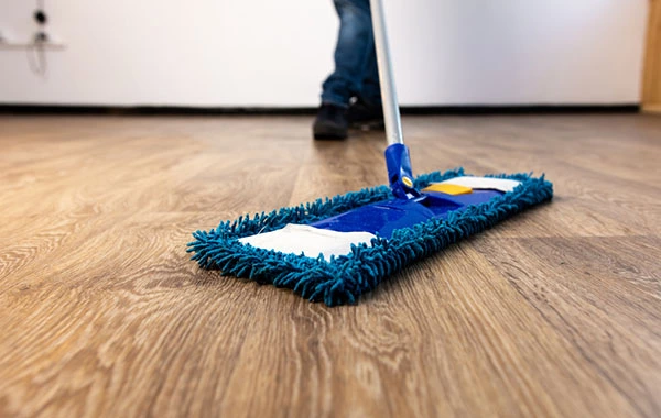 Man carefully damp mopping a prefinished hardwood floor with a cleaning solution.